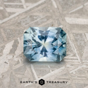 A radiant light yellow Montana sapphire, weighing 1.09 carats, is showcased on a textured, geometric-patterned surface. The gemstone features an intricate cut, displaying vibrant hues of yellow. The logo "Earth’s Treasury" is visible at the bottom of the image.