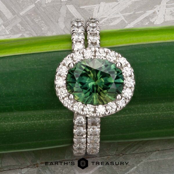 The Classic Pave Halo Ring in 14k white gold with 1.88-Carat Australian Sapphire, alongside the classic pave band in 14K white gold The Classic Pave Halo Ring in 14k white gold with a 1.88-carat Australian Sapphire and a matching pave band, displayed on a green leaf with the Earth's Treasury logo below.