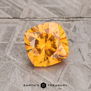 A 1.27-Carat Spessartine Garnet, with its enchanting orange square-cut facets, rests on a textured gray surface.