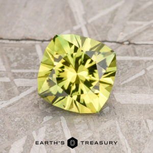 A faceted, square-shaped 2.74-carat lime green Australian sapphire rests on a textured, metallic surface. The surface has an intricate, geometric pattern with various intersecting lines and shapes. The text "EARTH'S TREASURY" appears at the bottom of the image.