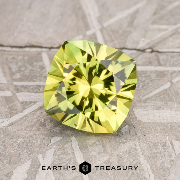 A faceted, square-shaped 2.74-carat lime green Australian sapphire rests on a textured, metallic surface. The surface has an intricate, geometric pattern with various intersecting lines and shapes. The text "EARTH'S TREASURY" appears at the bottom of the image.