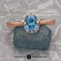 A rose gold ring, “2022-01-10 11-08-56 (B,Radius1,Smoothing1)-1200-BW,” with an oval blue gemstone on rough blue stone and the "Earth's Treasury" logo—ideal for Demeter Solitaire fans or lovers of classic solitaire elegance.