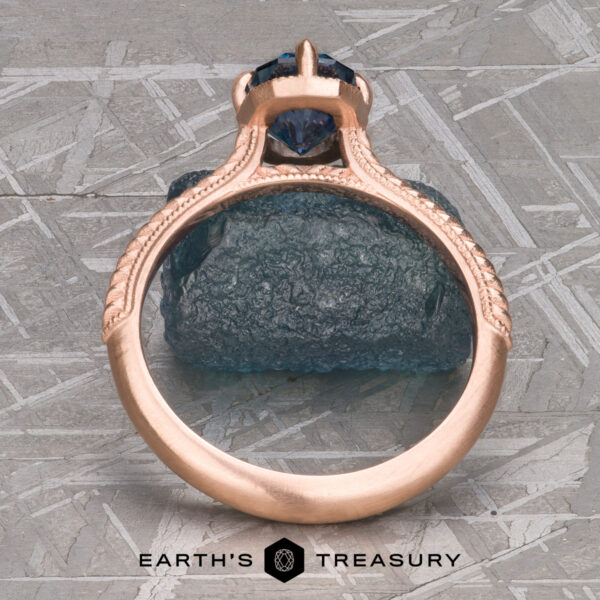 The “Demeter” Ring in 14k rose gold with 1.18-Carat Montana Sapphire The ring "2022-01-10 11-13-01 (B,Radius1,Smoothing1)-1200-BW" stands before a rough blue stone, with "EARTH'S TREASURY" and a hexagon logo below, evoking the timeless allure of a solitaire game.