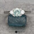 The "Aurelia" ring in 14k white gold showcases a central light green Montana sapphire weighing 1.05 carats, accented by two clear side stones, all set against an elegantly textured finish.