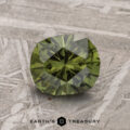 A 1.78-carat dark olive green Australian sapphire with a cushion cut is showcased on a textured metallic surface, featuring the "Earth's Treasury" text at the bottom.