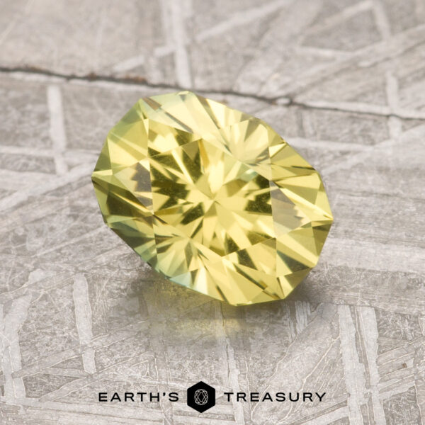 1.72-Carat Lemon Yellow Australian Sapphire A 1.72-carat Lemon Yellow Australian Sapphire, faceted in an oval shape, is shown on a textured gray surface with the "Earth's Treasury" logo beneath it.