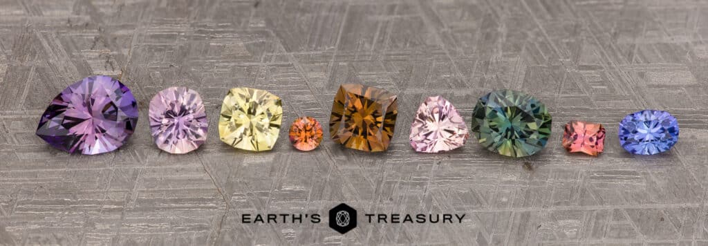 A row of variously colored gemstones, featuring vibrant purple, yellow, orange, green, and blue stones—including a breathtaking tanzanite—arranged on a textured grey background with the text "Tanzanite Family Photo content" at the bottom.
