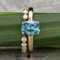 The “Freya” ring in 14k yellow gold with a 2.27-carat Montana sapphire is paired with the “Andelle” open band in 14k yellow gold, both displayed on a green leaf.