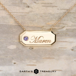 Stacked from 16 images. Method=B (R=1, S=1)" gold keepsake necklace with "Maren" engraved on the pendant and a small gemstone, showcased on light wood. "Earth's Treasury" logo appears at the bottom.