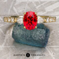 The "Galina" ring in 18k yellow gold showcases a 1.34-carat Spinel, elegantly set and displayed on rough blue-green mineral, with the Earth's Treasury logo at the bottom.