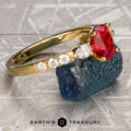 The "Galina" ring in 18k yellow gold with a 1.34-carat Spinel and three round diamonds rests on rough blue stone; the "Earth's Treasury" logo appears below, highlighting this striking jewelry piece.