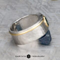 The "Armando" ring with a 1.57-carat Montana sapphire, featuring a wide silver band and gold accent, is displayed on a raw blue stone with the Earth's Treasury logo at the bottom.
