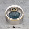 The "Armando" ring, crafted in silver and gold with a 1.57-carat Montana sapphire, stands upright framing a raw blue mineral on a textured gray surface. The "Earth's Treasury" logo appears below.