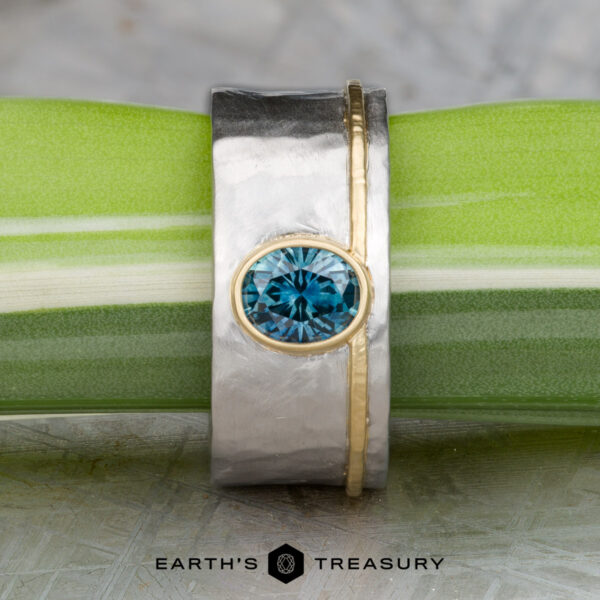 The "Armando" ring with 1.57-carat Montana sapphire The "Armando" ring features a 1.57-carat round Montana sapphire set in silver and gold, displayed on a green and white stem with the Earth’s Treasury logo below.