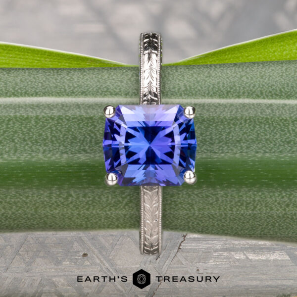 The Engraved "Cathedral" ring in 14K white gold with a 2.75-carat square-cut Tanzanite is displayed vertically against a green plant, with the "Earth's Treasury" logo at the bottom.