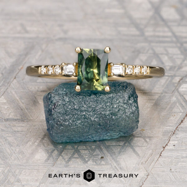 The "Fiona" ring in 14K yellow gold with 1.03-carat Australian sapphire A gold Arsenault, Ben *intl ring featuring a rectangular green gemstone and small diamonds on the band, displayed on a raw blue stone, with the "Earth's Treasury" logo below.