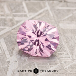 A 1.87-carat Lilac Pink Mahenge Garnet is elegantly showcased on a textured gray surface, with the text "Earth's Treasury" appearing at the bottom.