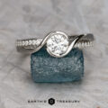 The "Faye" ring in platinum featuring a 0.71-carat lab diamond rests on a rough blue gemstone, with the "Earth's Treasury" logo shown below.