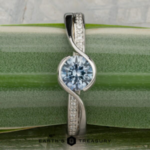 The "Faye" ring in platinum features a 0.92-carat Montana sapphire as its centerpiece and is displayed vertically on a green, striped leaf.