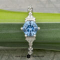 The "Morrigan" platinum ring, featuring a 1.64-carat hexagonal Montana sapphire and two triangular clear stones, is displayed on a green leaf.