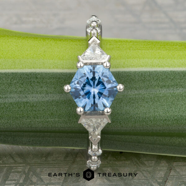 The "Morrigan" ring in platinum with 1.64-carat Montana sapphire The "Morrigan" platinum ring, featuring a 1.64-carat hexagonal Montana sapphire and two triangular clear stones, is displayed on a green leaf.