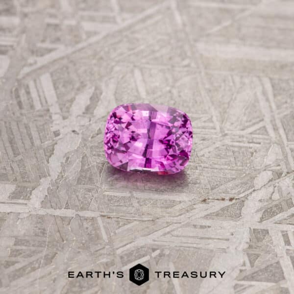1.13-Carat Purplish Pink Madagascar Sapphire A vibrant 1.24-carat pink Madagascar sapphire with a rectangular cushion cut is placed on a textured, metallic background. The stone sparkles with light reflections, and beneath it is the text "EARTH'S TREASURY" accompanied by a geometric logo.