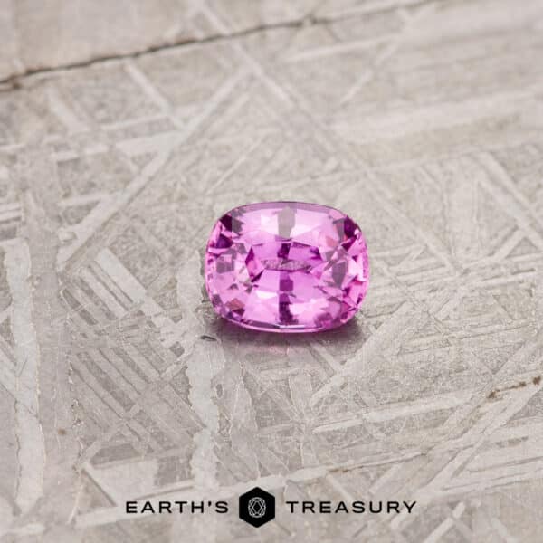 0.98-Carat Hot Pink Madagascar Sapphire A 1.24-carat cushion-cut pink Madagascar sapphire displayed on a textured metallic surface. The bottom of the image features the logo and text "Earth's Treasury.