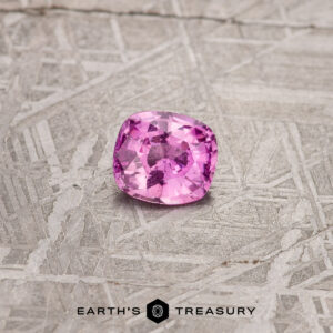 The 1.08-Carat Hot Pink Madagascar Sapphire, in a cushion cut, beautifully rests on a textured gray surface.