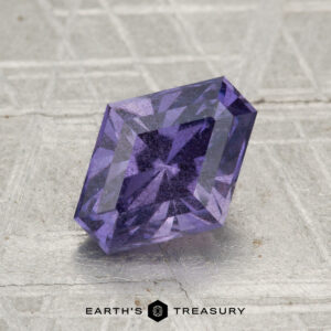 The 2.38-Carat Purple Umba Sapphire, cut in a rectangular faceted shape, rests on a textured surface with "EARTH'S TREASURY" displayed at the bottom.