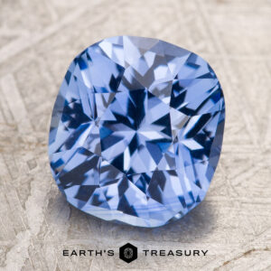 A 4.53-carat sky blue Ceylon sapphire (heated) with a cushion cut rests on a textured gray surface, with "EARTH'S TREASURY" and a geometric logo displayed at the bottom.