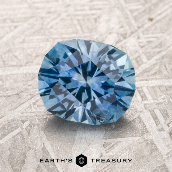 1.74-Carat Sky Blue Montana Sapphire (Heated) A 1.74-carat sky blue Montana Sapphire (heated), cut in a round brilliant style, is displayed on a textured surface with the text "Earth's Treasury" below it.
