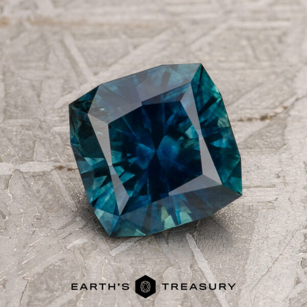 1.81-Carat Deep Blue-Green Montana Sapphire (Heated) A 1.81-carat deep blue-green heated Montana Sapphire is displayed on a textured gray surface with "EARTH'S TREASURY" written below.