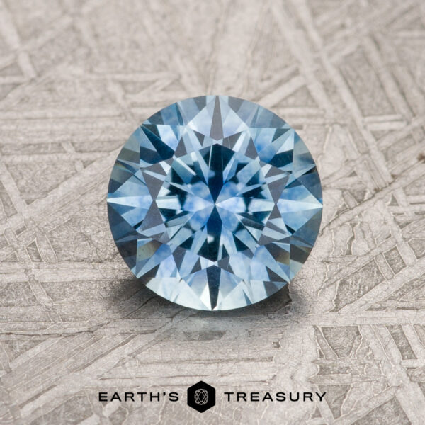 1.37-Carat Sky Blue Montana Sapphire (Heated) 1.37-Carat Sky Blue Montana Sapphire (Heated) in a round brilliant cut, displayed on a metallic textured surface with the "Earth's Treasury" logo and text below the gemstone.