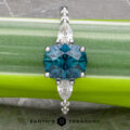 The "Carina" ring in 14k white gold, featuring a 1.53-carat Montana Sapphire flanked by marquise-cut gems, is displayed on a green plant stem. The "Earth's Treasury" logo appears at the bottom, enhancing its elegance.