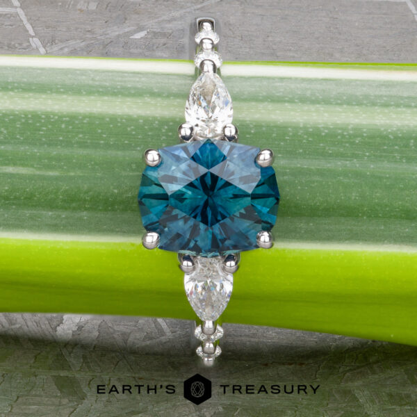 The "Carina" ring in 14k white gold with 1.53-Carat Montana Sapphire The "Carina" ring in 14k white gold, featuring a 1.53-carat Montana Sapphire flanked by marquise-cut gems, is displayed on a green plant stem. The "Earth's Treasury" logo appears at the bottom, enhancing its elegance.