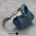 A "Carina" ring in 14k white gold with a 1.53-carat Montana sapphire is displayed on a rough blue stone, with the Earth's Treasury logo beneath.