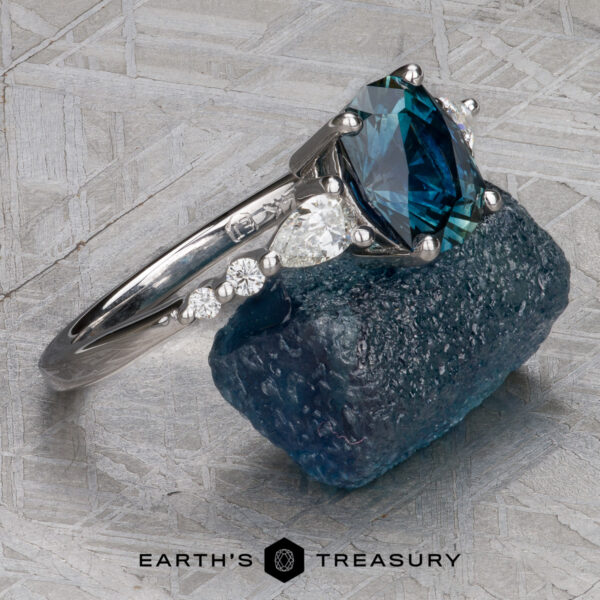 The "Carina" ring in 14k white gold with 1.53-Carat Montana Sapphire A "Carina" ring in 14k white gold with a 1.53-carat Montana sapphire is displayed on a rough blue stone, with the Earth's Treasury logo beneath.