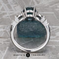 A "Carina" ring in 14k white gold with a 1.53-carat Montana sapphire is shown upright from the side on a textured surface, featuring the "Earth’s Treasury" logo at the bottom.