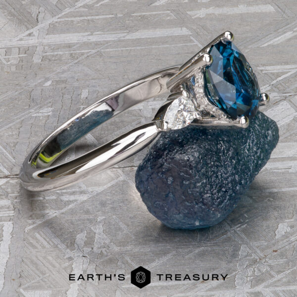 The Minimal "Avalon" ring in 18k white gold with 1.69-Carat Montana sapphire The Minimal "Avalon" ring in 18k white gold with a 1.69-carat Montana sapphire is displayed on a rough blue mineral, with the "Earth's Treasury" logo below.