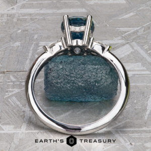 A minimal ring with a large blue gemstone, "Stacked from 61 images. Method=B (R=1,S=4)", is displayed upright before a matching rough blue stone on a textured grey surface. The "EARTH'S TREASURY" logo appears below.