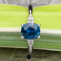 The "Stacked from 61 images. Method=B (R=1,S=4)" pendant features a round blue gemstone with two marquise-cut clear stones, evoking a three-stone ring, set against a green and white leafy background.