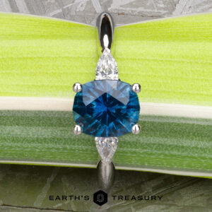 The "Stacked from 61 images. Method=B (R=1,S=4)" pendant features a round blue gemstone with two marquise-cut clear stones, evoking a three-stone ring, set against a green and white leafy background.