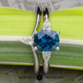 The Minimal "Avalon" ring in 18k white gold features a 1.69-carat Montana sapphire center stone with two white pear-shaped side stones, shown resting on a green leaf.