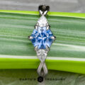 A pendant inspired by the "Elowen" ring in platinum, which features a 1.09-carat Montana sapphire at its center, flanked by two white pear-shaped stones, is elegantly set and displayed on a green striped leaf.