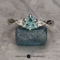 The "Elowen" ring in 14K white gold with a 1.06-carat Montana sapphire and two accent stones, shown on a rough blue crystal with the "Earth's Treasury" logo below.