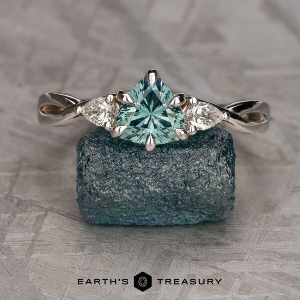 The "Elowen" ring in 14K white gold with 1.06-carat Montana sapphire The "Elowen" ring in 14K white gold with a 1.06-carat Montana sapphire and two accent stones, shown on a rough blue crystal with the "Earth's Treasury" logo below.