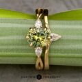 The "Elowen" ring in 18K yellow gold features a 2.13-carat Australian sapphire center with three pear-shaped white accent stones, shown with the "Laita" band in 18K yellow gold. Displayed on a leaf with the "Earth's Treasury" logo at the bottom.