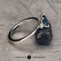 The "Alocasia" ring in 18K white gold features a 1.00-carat rectangular Montana sapphire and two round diamonds, shown atop a rough blue crystal with the "Earth's Treasury" logo below.