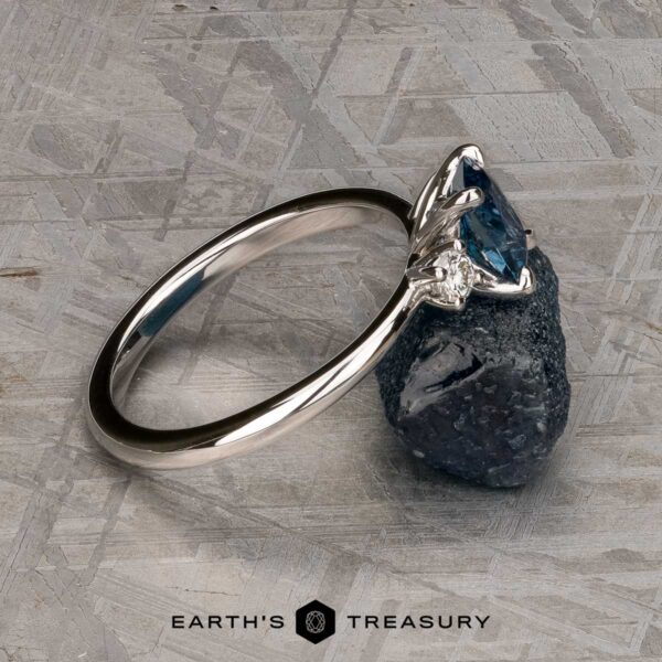 The "Alocasia" ring in 18K white gold with 1.00-carat Montana sapphire The "Alocasia" ring in 18K white gold features a 1.00-carat rectangular Montana sapphire and two round diamonds, shown atop a rough blue crystal with the "Earth's Treasury" logo below.