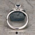 The "Alocasia" ring in 18K white gold features a 1.00-carat rectangular Montana sapphire and two round diamonds, shown atop a rough blue crystal with the "Earth's Treasury" logo below.